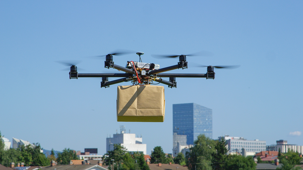 Fliegende Drohne mit Paket vor Stadt-Skylline